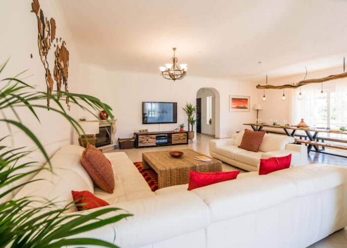 lounge large leaving room with white sofa, red pillows and TV in a surf house near Lagos
